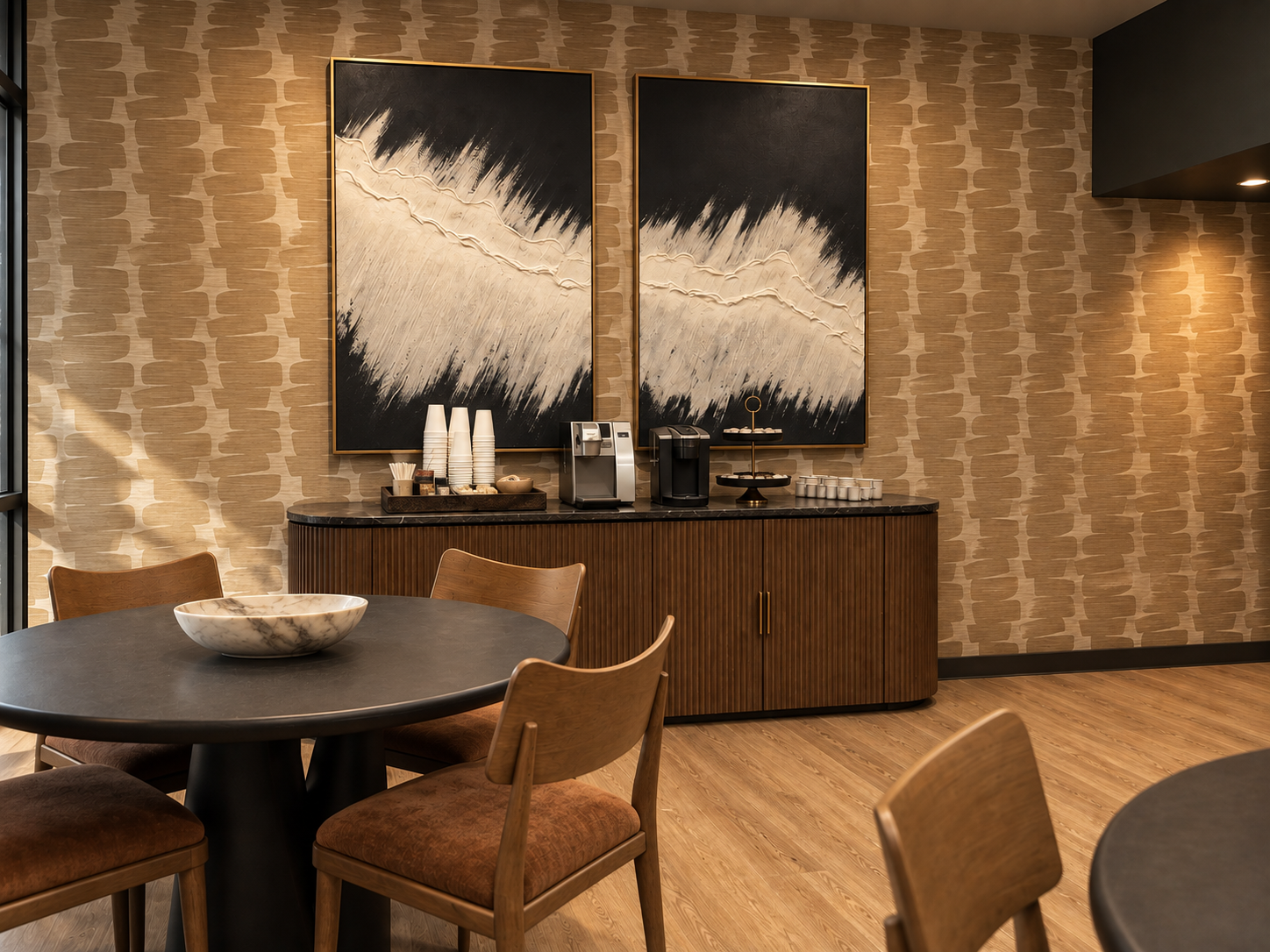 A workplace coffee bar with patterned wallcovering, black and white abstract art and warm wood cabinetry
