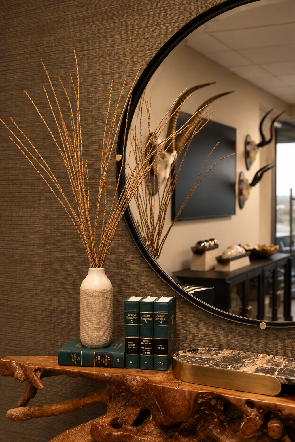 A sculptural burl wood console styled with books and a vase beneath a large round mirror
