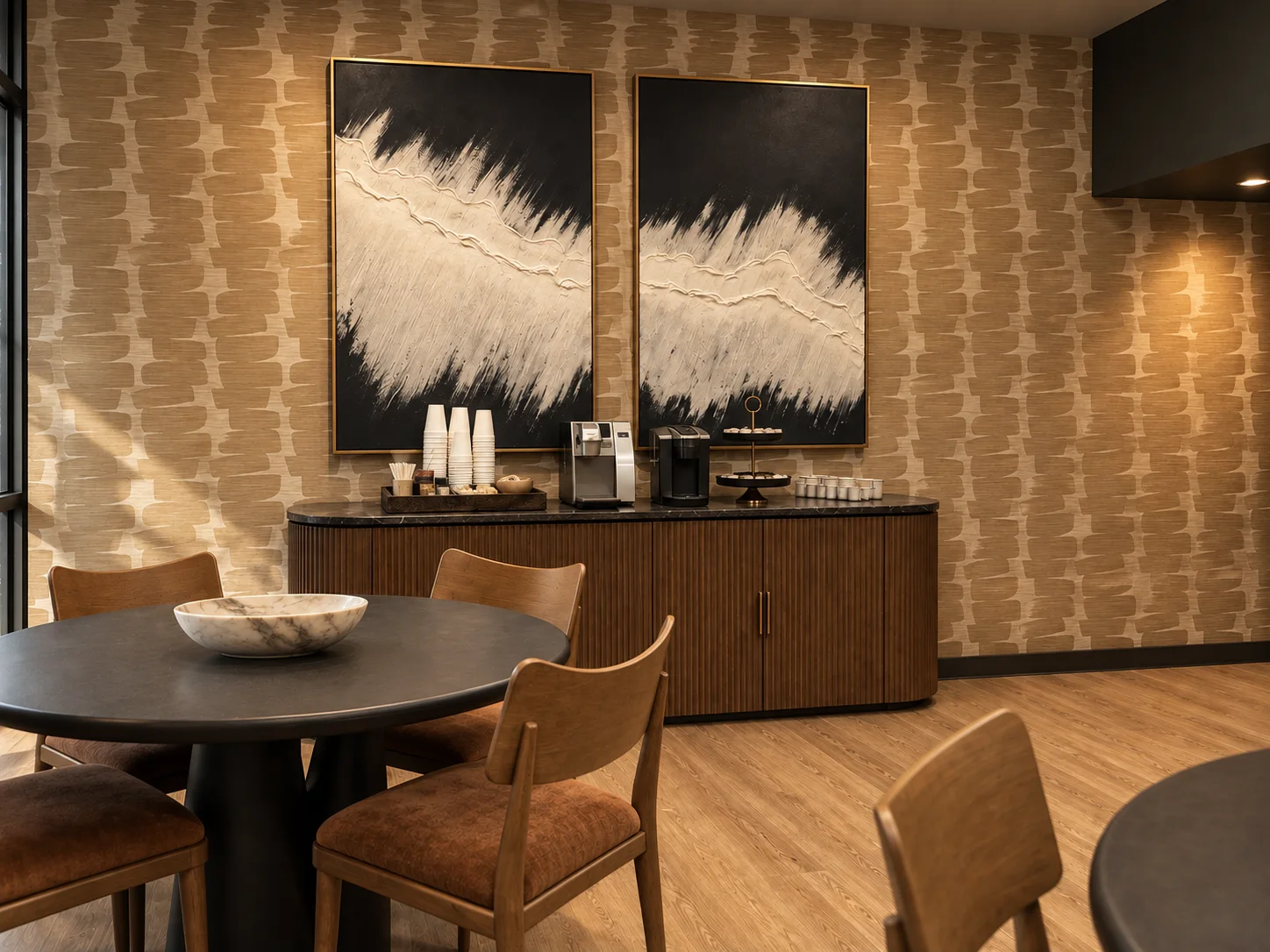 A workplace coffee bar with patterned wallcovering, black and white abstract art and warm wood cabinetry
